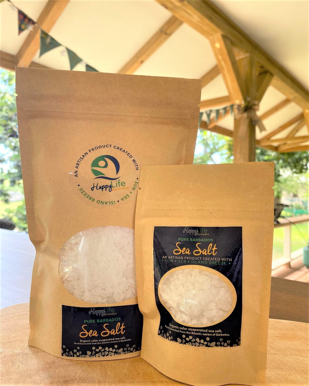 Two different sized packages of sea salt on a table with tropical background under awning